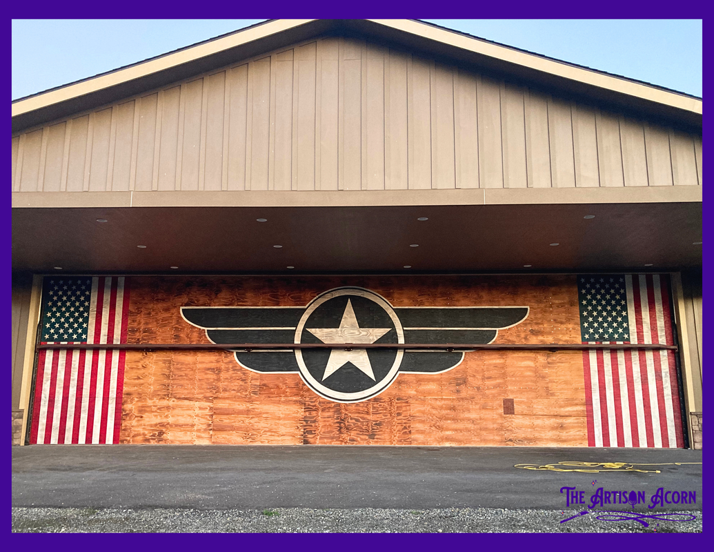 Americana mural painted on airplane hanger door. Includes two American flags, and a vintage air force logo. Painted as a wash to allow the beauty of the wood grain to show through.